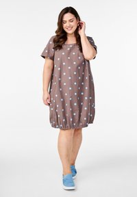 Braunes Kleid mit Polka-Dots, kurzen Ärmeln, elastischem Saum und hellblauen Punkten. Kombiniert mit blauen Slippers für einen lässigen Look.