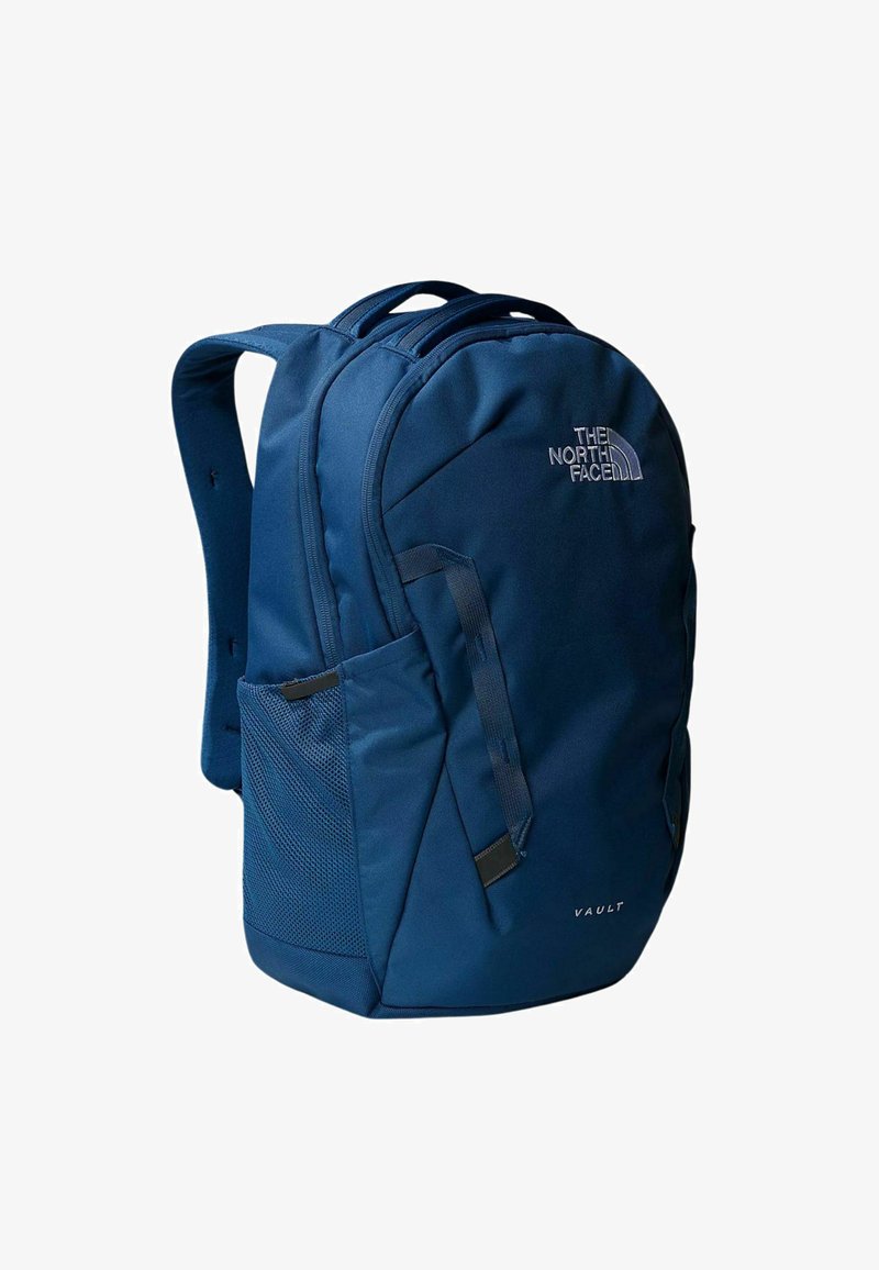 Marinblå ryggsäck gjord av slitstarkt tyg, med vadderade axelremmar, en mesh sidoficka och North Face-logotyp. Modell: Vault.