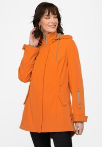 Oranssi hupullinen takki, jossa on sileä pinta, vetoketjulliset taskut ja epäsymmetrinen helma. Varustettu harmailla nyöreillä ja reunuksilla.