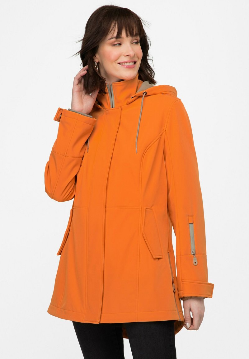 Oranssi hupullinen takki, jossa on sileä pinta, vetoketjulliset taskut ja epäsymmetrinen helma. Varustettu harmailla nyöreillä ja reunuksilla.