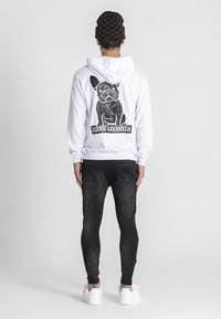 Biely kapucňový sveter s čiernou grafikou francúzskeho buldoga a textom "GIANNI KAVANAGH", spárovaný s čiernymi džínsami a bielymi teniskami.