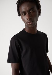 Tricou negru cu mânecă scurtă, realizat din bumbac moale, cu un guler clasic tip crew și o croială lejeră.