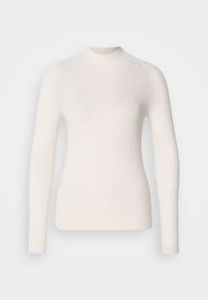 Valge ribaga pikkade varrukatega topp, millel on kõrge kaelus. Omab stiilset lõiget ja kerget logo detaili rinnal. Sile tekstuur.