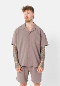 Hellbraunes Kurzarmhemd mit Tasche, Knöpfen und Reverskragen, kombiniert mit passenden Shorts. Weicher Stoff und lockere Passform.
