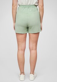 Grønne, teksturerte shorts med et elastisk livbånd som rekker midt på låret, og kombinert med hvite sneakers. Bakre visning; ingen lommer synlige.