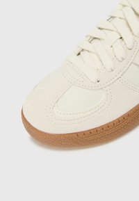 Kreemivärvi sneakers tekstuurse kummi tallaga, mis on valmistatud sametist ja siledast nahast, ning lame paelaga. Kaarduv disain koos õmblusdetailidega.