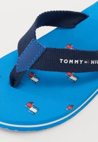 Blå flip-flop med marineblå stoffstropp, med logo og små flagg mønstre på sålen. Glatt tekstur og gummisåle.