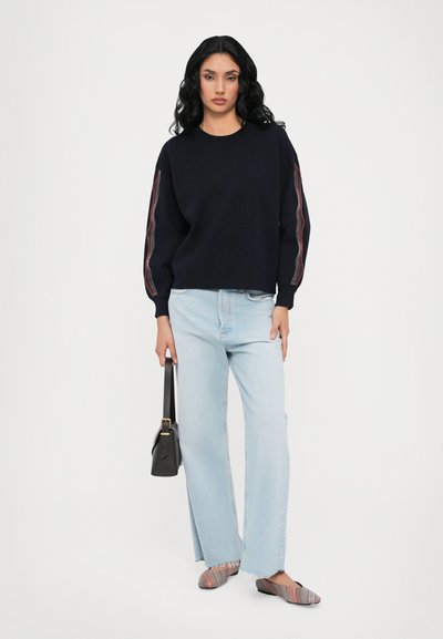 Navy sweater with puffed sleeves and striped accents, paired with light blue wide-leg jeans and multicolored striped flats.