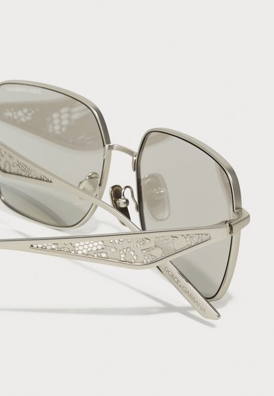 Metāla saulesbrilles ar pelēkiem stikliem, sarežģītu izgriezumu dizainu uz kājām un zīmolu "DOLCE & GABBANA" iegravētu uz tempļa.