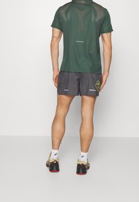 Green mesh athletic t-shirt with short sleeves, paired with black checkered shorts featuring a neon accent and reflective details.