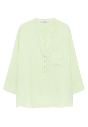 Blouse jaune pâle à manches longues, avec un col en V, une courte patte de boutonnage et une poche poitrine, sur fond blanc.