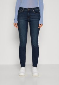 Mörkblå skinny jeans i denim, med fem fickor, dragkedja och subtila sömnadsdetaljer. Bärs med vita sneakers.