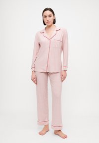 Conjunto de pijama listrado em vermelho e branco com parte superior abotoada e bolso, mangas longas e calças combinando com bainhas ajustadas. Tecido leve.