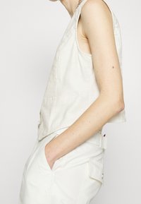 Linne ärmlös topp i off-white med sidofickor och avslappnad passform, tillsammans med matchande byxor med knapprad.