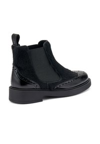 Botas de tobillo negras que combinan cuero liso y piel texturizada, con paneles laterales elásticos y un intrincado detalle de brogue.