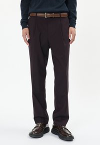 Sötét bordó nadrág, pleat-el, sima tapintással, és barna bőrövvel. Fényes barna cipővel párosítva.