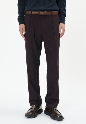 Pantaloni bordeaux închis cu plii, textură netedă și o curea din piele maronie. Asortați cu pantofi maro lucioși.