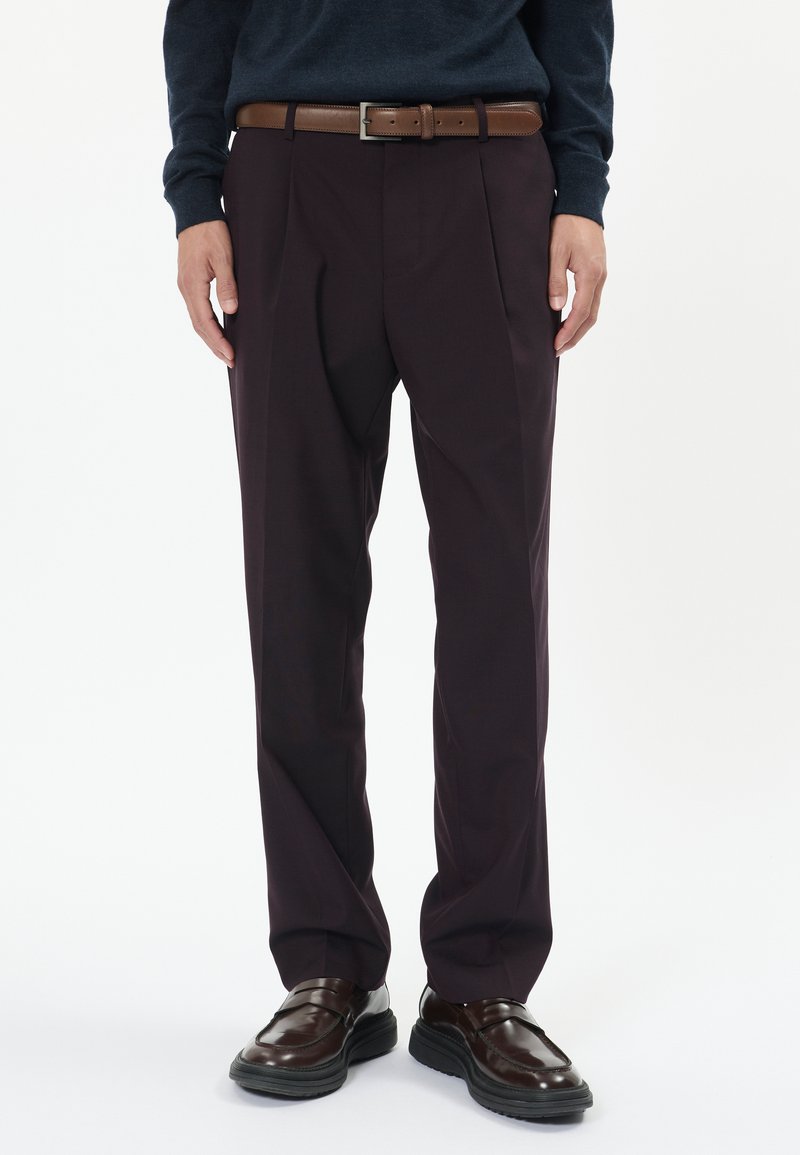 Sötét bordó nadrág, pleat-el, sima tapintással, és barna bőrövvel. Fényes barna cipővel párosítva.