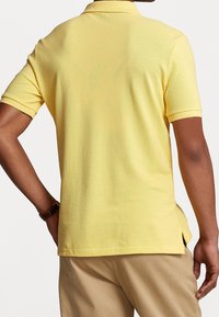 Yellow cotton polo shirt with short sleeves, ribbed collar, and side slits, showcasing a textured fabric and casual design.