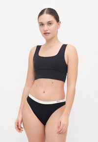 Black crop top with a square neckline paired with black high-waisted bikini bottoms featuring a white waistband and three button accents.