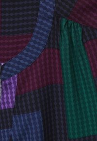 Flerfärgad tyg med geometriska mönster i nyanser av lila, grön, marinblå och svart. Har en strukturerad yta och kurviga sömmar.