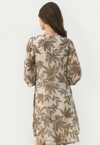 Kurzärmliges Kleid in hellbeige mit braunen Blattmustern, mit runden Ausschnitt und leicht gerafften Schultern. Weicher, fließender Stoff.