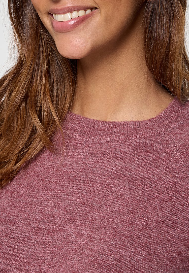 Maglione rosa chiaro con scollo rotondo, morbido al tatto e dettagli a costine al colletto, indossato da un modello sulla parte superiore del corpo.