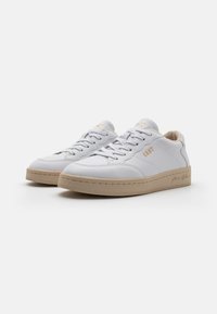 Vita lädersneakers med en beige gummisula, med stuckna detaljer och en guldprägling av logotypen på sidan och tungan.