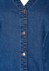 Denim odjevni predmet s dubokim V-izrezom, pet bakrenih dugmadi i kontrastnim šavovima na teksturiranoj plavoj tkanini.