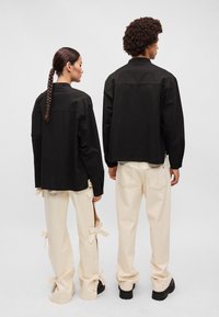 Juodas, ilgomis rankovėmis marškinėliai su laisvu siluetu, derinami su grietinėlės spalvos plačiadrugiais keliais, turinčiais juostelės rišimo detales siūlėse.