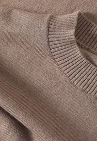 Pull en tricot marron clair avec une surface texturée et un col côtelé. Le tissu semble doux et confortable, avec une finition lisse.