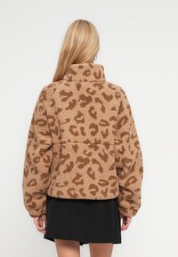 Καφέ φλίς μπουφάν με λεοπάρ σχέδιο, ψηλό γιακά, μακριά μανίκια και υφή υφάσματος. Διαθέτει άνετη εφαρμογή και ραφές με λεπτομέρειες.