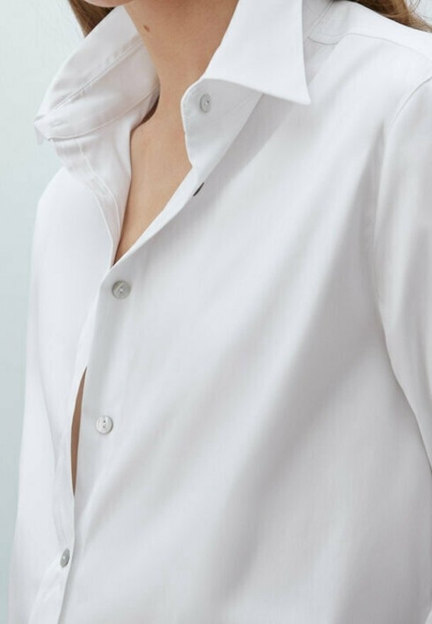White collared shirt, buttoned at the neck, made of smooth fabric, featuring a relaxed fit and slightly open front with a crisp collar.