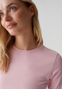 Hellrosa langärmliges Oberteil mit rundem Ausschnitt. Glatter, figurbetonter Jersey-Stoff mit dezentem Glanz und minimalen Nahtdetails.