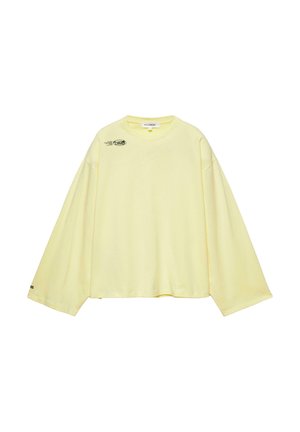 Svetložlté tričko s dlhými rukávmi a okrúhlym výstrihom, s nadrozmernými rukávmi a malým čiernym nápisom na ľavej hornej časti hrudníka a na ľavom manžete.