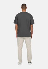 Gray cotton t-shirt with short sleeves, relaxed fit, paired with light beige pants and white sneakers, viewed from the back.