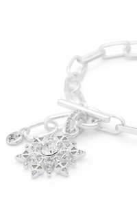 Söljekedjearmband med en stjärnexplosionpendel som har en central klar sten, triangulära detaljer och intrikata mönster runt kanterna.