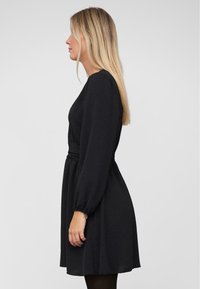 Vestido negro de manga larga con cintura ajustada, falda suelta y tejido suave. Presenta mangas fruncidas y cae por encima de la rodilla.