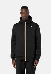 Sort zip-up hoodie med snøre i hætten, med en hvid og gul stribet lynlås og et lille logo på venstre bryst. Blødt stof.