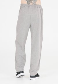 Graue Baumwoll-Sweatpants mit einem elastischen Bund, geraden Beinen und umgeschlagenen Säumen, kombiniert mit schwarzen Sportschuhen.