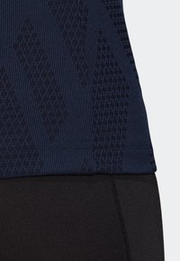 Marinblå träningslinne med texturerade mönster, som har en ribbad fåll. Kombinerat med svarta tights för en figurnära look.