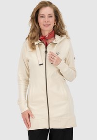 Beige Kapuzenpullover mit Reißverschluss, einer Kapuze und vorderen Taschen. Verfügt über Kordeln, gerippte Bündchen und ein Herz-Logo auf der Brust. Weiches Material.
