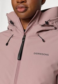 Roze waterdichte jacket met een hoge kraag, verstelbare trekkoordcapuchon, ritsen en zwarte branding op de borst. Soepele, matte textuur.