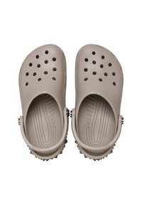 Beige Clogs aus strukturiertem Gummi, mit mehreren Löchern, einem Riemen hinten und stacheligen Details entlang der Ferse für zusätzlichen Halt.