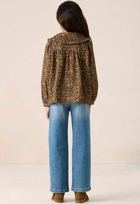 Brown leopard print blouse with a large collar, gathered sleeves, and a loose fit, paired with light blue wide-leg jeans and brown ankle boots.
