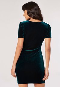 Robe en velours vert foncé à manches courtes, silhouette ajustée, texture lisse et décolleté rond. Présentée de dos.