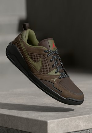 Brązowo-zielony sneaker Nike Air Jordan z czarną podeszwą i wzorzystymi sznurowadłami, unoszący się nad kamienną powierzchnią na ciemnym tle.
