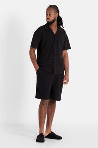 Zwarte korte mouwen shirt met een zak, gecombineerd met zwarte shorts en instap schoenen, met een eenvoudig ontwerp en lichtgewicht stof.