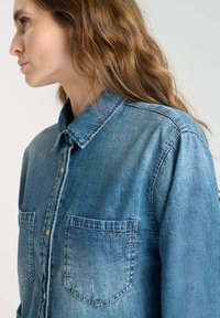 Denim shirt, light blue, long sleeves, button-down collar, front pockets, subtle stitching detail on pockets, relaxed fit.