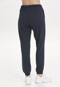 Marineblaue Jogginghosen mit elastischem Bund und umsäumten Knöcheln, ausgestattet mit seitlichen Taschen und einem weichen, glatten Stofftextur.